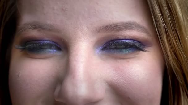 Close-up tiro de jovem bela cara feminina com olhos olhando para a câmera sorrindo alegremente com maquiagem deslumbrante com fundo isolado em preto — Vídeo de Stock