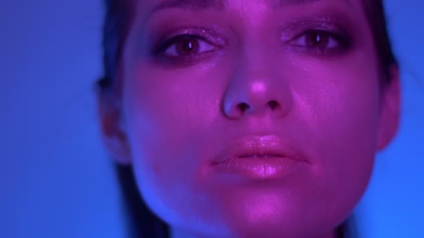 Mode unga modell i färgglada lila och blå neonljus poserar i kameran i studion. — Stockvideo