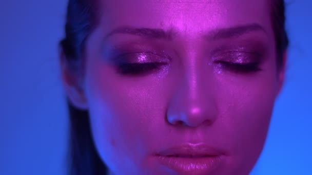 Niezwykły model mody w kolorowych purpurowych i niebieskich neonowych świateł stwarzających do kamery w studiu oglądanie rightwards. — Wideo stockowe