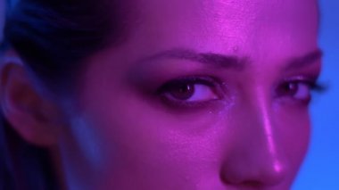 Renkli mor ve mavi neon ışıklar profil fütüristik moda modeli stüdyoda kameraya dikkatle izliyor.