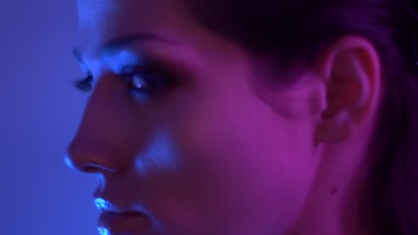 Futuristic fashion model in colorful neon lights turns to camera and watches seriously and fixedly into it in studio. — Stock Video
