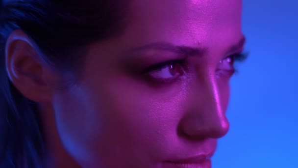 Modelo de moda futurista en coloridas luces de neón púrpura y azul mirando con misteriosa sonrisa en la cámara en el estudio . — Vídeo de stock