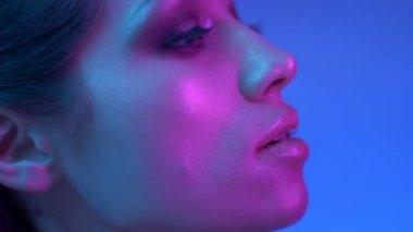 Renkli neon ışıklar profil parlak moda modeli yavaş yavaş sağa ve stüdyoda kamera içine izlerken.