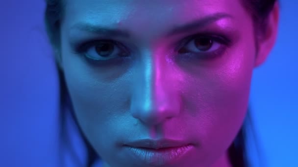 Modelo de moda em luzes de néon roxo e azul coloridas posando lentamente e assistindo atentamente na câmera em estúdio . — Vídeo de Stock