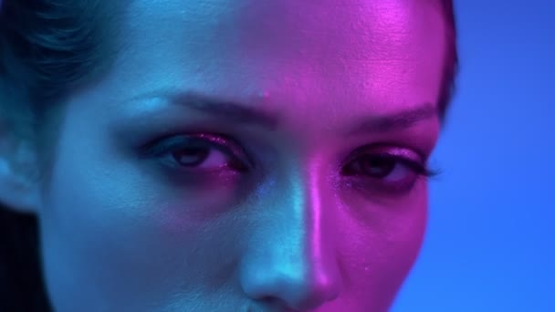 Futuristische mode model met glitter Eye-Shadows in kleurrijke neonlichten draait naar camera en horloges bewaring in het. — Stockvideo