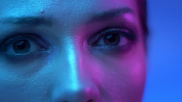 Närbild av extraordinära mode modell med glitter makeup i färgglada neonljus blinkande i kameran i studion. — Stockvideo