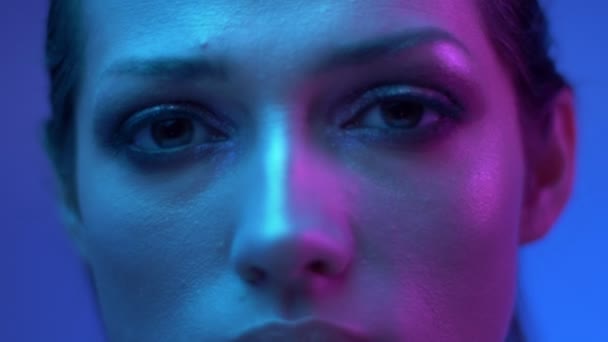 Fashion model in colorful purple and blue neon lights watching with fixed and serious glance into camera in studio. — Stock Video