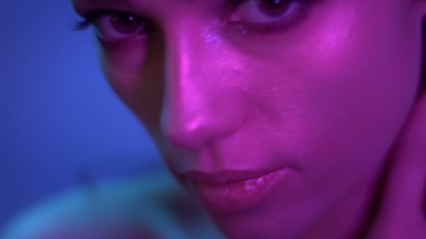 Kosmisk mode modell i lila neonljus rör sig långsamt och tittar uppmärksamt i kameran i studion. — Stockvideo