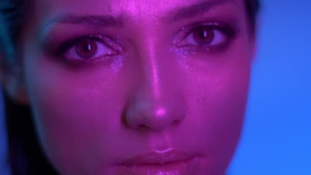 Kosmický módní model v purpurově neonové světlech se pomalu pohybuje a dívá se vážně někde ve studiu. — Stock video