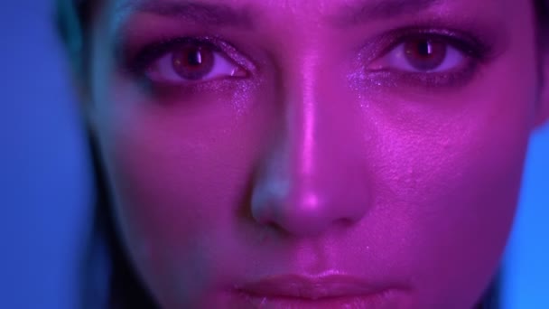 Modelo de moda cósmica con maquillaje de brillo en luces de neón púrpura parpadeando y mirando tranquilamente a la cámara en el estudio . — Vídeo de stock