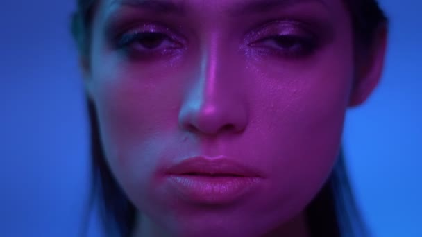 Fantastische mode model met glitter make-up in paarse neonlichten kijken zeker in de camera in Studio. — Stockvideo