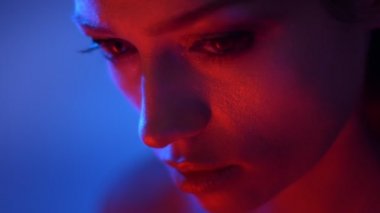 Kırmızı ve mavi neon ışıklar fantastik moda modeli nin yakın çekim dikkatle kameraya aşağıdan saatler.