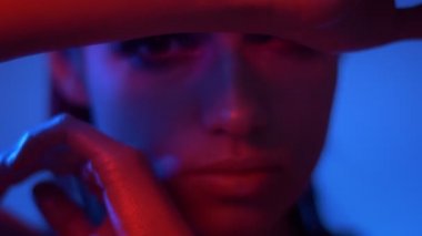 Kırmızı ve mavi neon ışıklar fütüristik moda modeli yakın çekim elleri ve kamera içine saatler ile yüz gizleme.
