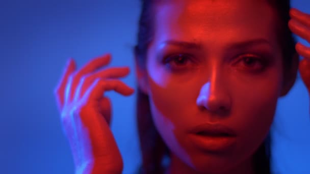 Modelo de moda futurista em luzes de néon vermelho e azul cobrindo rosto com as mãos estranhamente e olhando fixamente para a câmera . — Vídeo de Stock