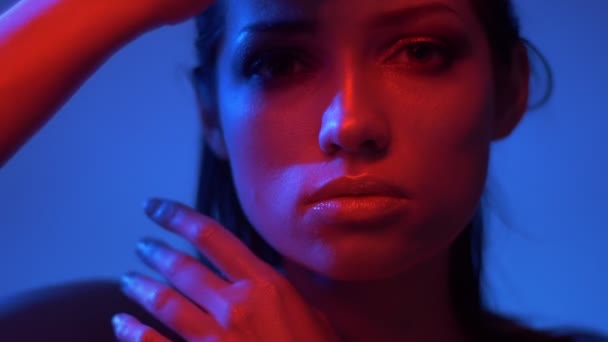 Futurisztikus divat modell piros és kék neonfények megható arcát kézzel óvatosan és pillantva nyugodtan a kamera. — Stock videók