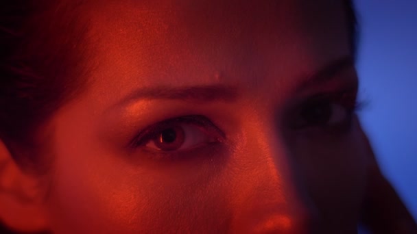Close-up Eye-portret van kalm mode model in rode neon licht te kijken bewaring met geen emoties in de camera. — Stockvideo