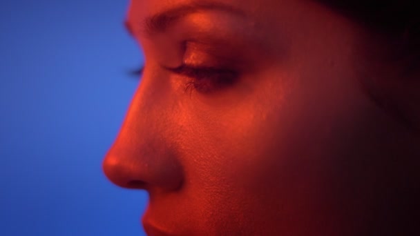 Close-up tiro no perfil dos olhos e lábios do modelo de moda sendo sério na luz de néon vermelho no fundo azul . — Vídeo de Stock