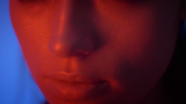 Close-up shoot van futuristisch mode model in rode neonlichten die haar handen over haar gezicht bewegen op een blauwe achtergrond. — Stockvideo