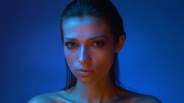 Mavi neon ışıklar glitter parlak makyaj ile parlak modeli stüdyoda esrarengiz kamera içine izlerken.