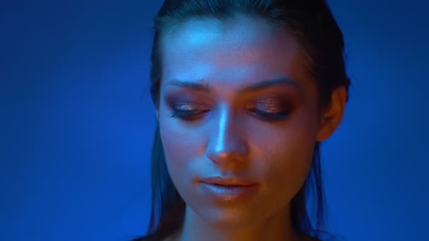 Modelo futurista com maquiagem brilhante brilho em luzes de néon azul movendo os olhos da esquerda para a direita misteriosamente no estúdio . — Vídeo de Stock