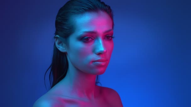 Modello futuristico con brillantini trucco lucido in luci al neon blu e rosa che muovono gli occhi da sinistra a destra in studio . — Video Stock