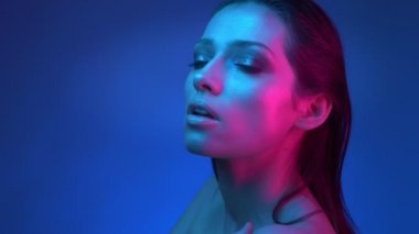 Mavi ve pembe neon ışıkları ile parlayan moda yıldızı sabit kameraya izlerken göğüs üzerinde ellerini geçti.