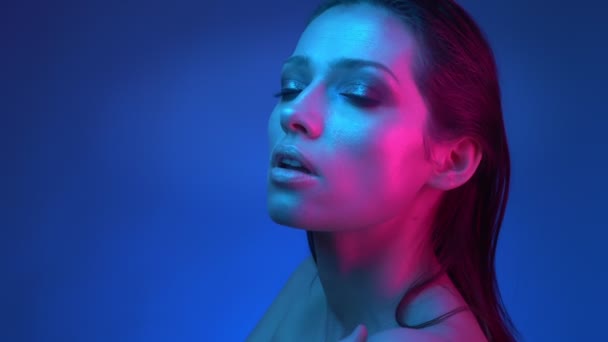 青とピンクのネオンライトで輝くファッションスターは、固定カメラに見て胸の上に彼女の手を横切った. — ストック動画