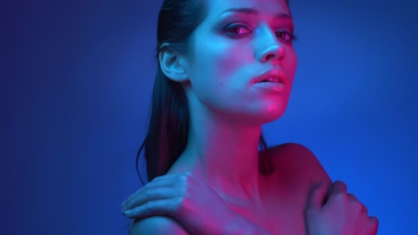 Brillante estrella de la moda con luces de neón azules y rosas posando en la cámara con las manos cruzadas sobre el pecho en el estudio . — Vídeo de stock