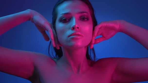 Extraordinära Fashion Star med glitter makeup i blått och rosa neonljus flyttar händerna över hennes ansikte poserar i kameran. — Stockvideo