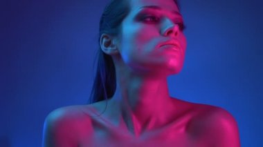 Mavi ve pembe neon ışıklar glitter makyaj ile parlayan model dikkatle sağdan izliyor ve kendini sarılma.