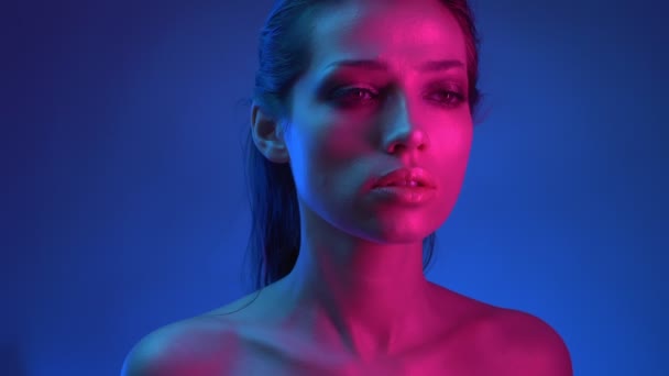 Glühender Modestar mit Glitzerschminke in blauen und rosafarbenen Neonlichtern, der nachdenklich in die Kamera blickt. — Stockvideo