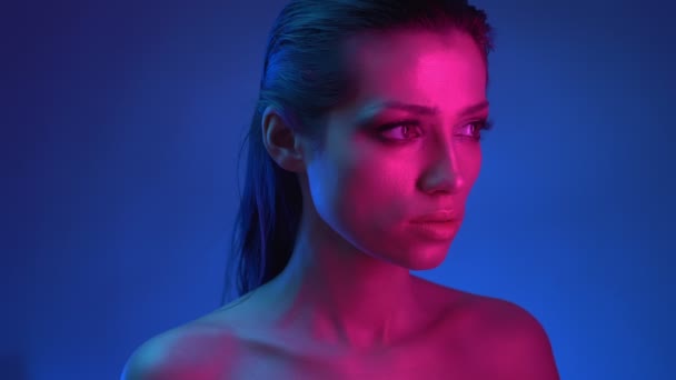 青とピンクのネオンライトでキラキラメイクでプロファイルで輝くファッションスターは、深く、思慮深く右に見て. — ストック動画