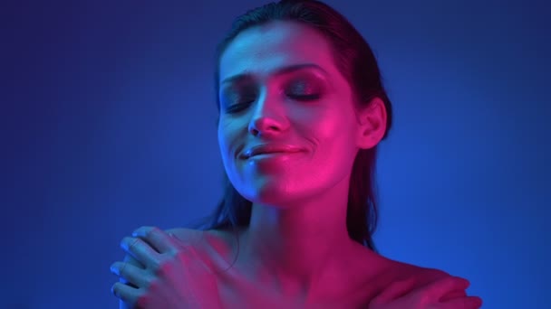 Modelo de moda brillante con maquillaje brillante en luces de neón azules y rosadas abrazándose y sonriendo alegremente . — Vídeo de stock