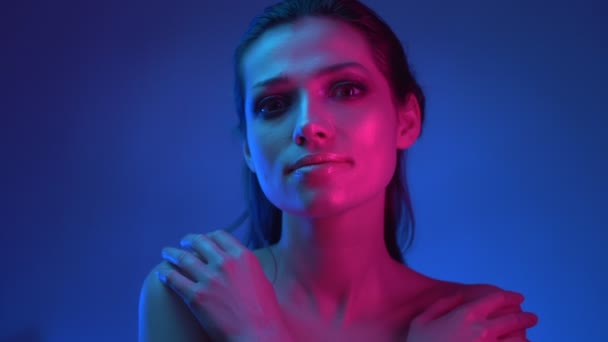 Lumineux modèle à la mode avec un maquillage pailleté dans les néons bleu et rose s'étreignant et regardant vers le haut de façon rêveuse . — Video