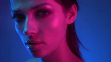 Mavi ve pembe neon ışıklar ciddi kameraya gözetleme glitter makyaj ile model profilinde yakın çekim.