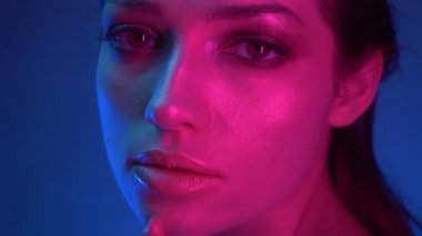 Mavi ve pembe neon ışıklarla ışıltılı makyajlı modelin yakın çekim slayt çekimi kameraya dokunuyor.