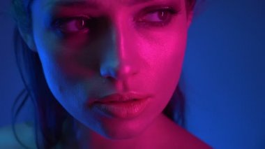 Mavi ve pembe neon ışıklı modelin yakın çekim leri, sağdan kameraya doğru ve huzurlu bir şekilde izler.