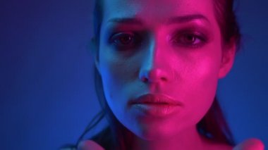Mavi ve pembe neon ışıklı güzel modelin gizemli bir şekilde ona ulaşan kameraya dikkatle bakması yakın çekim.