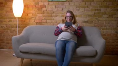 Kapalı bir evde rahat bir dairede kanepede otururken tablette tarama genç hamile kadın Closeup çekim