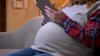 Kapalı bir rahat dairede kanepede otururken tablet kullanarak hamile kadın mide closeup ateş