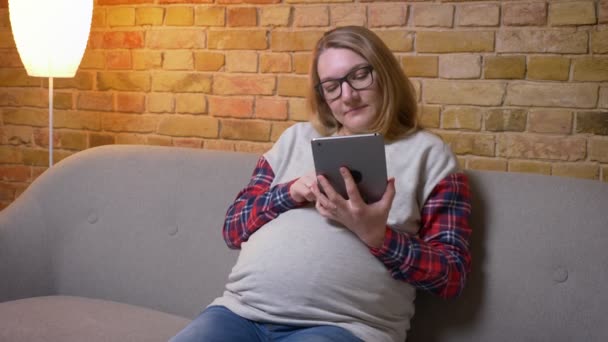 Rozstřílejte mladou těhotnou ženu pomocí tabletu a ukazovátko zelené obrazovky s fotoaparátem usmívaje se šťastně a sedí na pohovce v útulném bytě uvnitř — Stock video