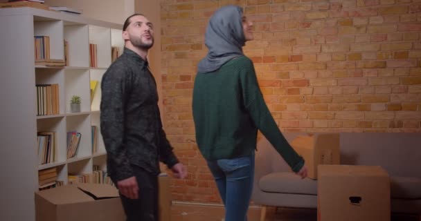 Primer plano de la joven pareja musulmana alegre caminando en un apartamento recién comprado e inspeccionando una habitación sonriendo felizmente — Vídeo de stock