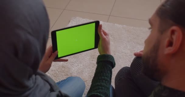 Primer plano de vista trasera de brote de joven pareja alegre musulmán en un apartamento recién comprado utilizando la tableta con pantalla verde — Vídeo de stock