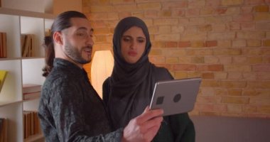 Tabletüzerinde bir görüntülü arama olan ve yeni satın alınan daire gösteren genç neşeli Müslüman çift Closeup ateş