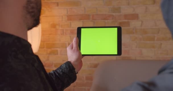 Närbild tillbaka Visa shoot av unga glada muslimska paret använda tabletten med grön skärm med reklam på den inomhus — Stockvideo