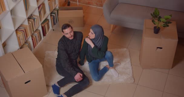 Closeup top shoot of young cheerful muslim couple sitting on the floor in a newly bought apartment smiling happily dreaming about how to furniture the room — Stock Video