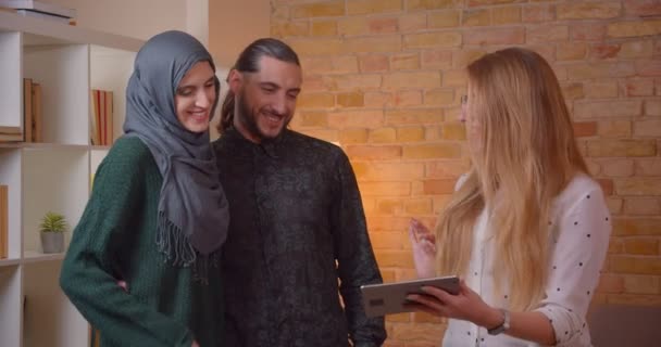 젊은 행복 한 무슬림 커플의 클로즈업 촬영 은 실내에서 유쾌하게 껴안고 새로 구입 한 아파트에 서있는 태블릿으로 재갈을 말하려고합니다. — 비디오