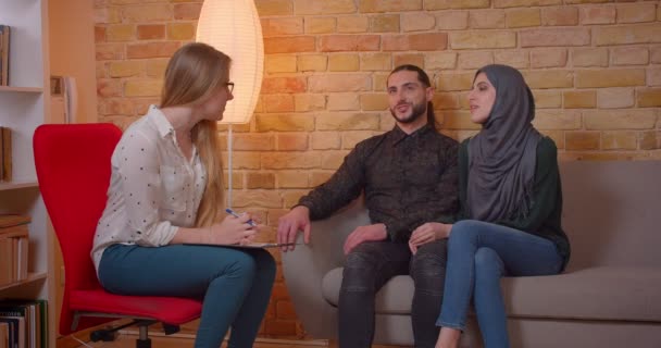 Closeup shoot of young happy muslim couple discussing with a realter a new apartment smiling cheerfully sitting on the couch — Stock Video