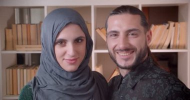 Genç mutlu Müslüman çift kamera düz bakarak ve gülümseyerek ve yeni satın alınan bir dairede neşeyle sarılma Closeup ateş