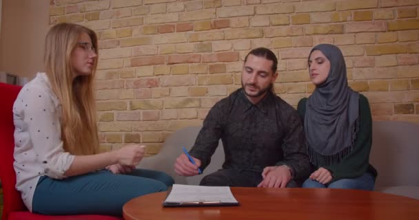 Kanepede oturan yeni bir daire satın alma konusunda bir realter ile anlaşma imzalayan genç mutlu Müslüman çift Closeup ateş — Stok video